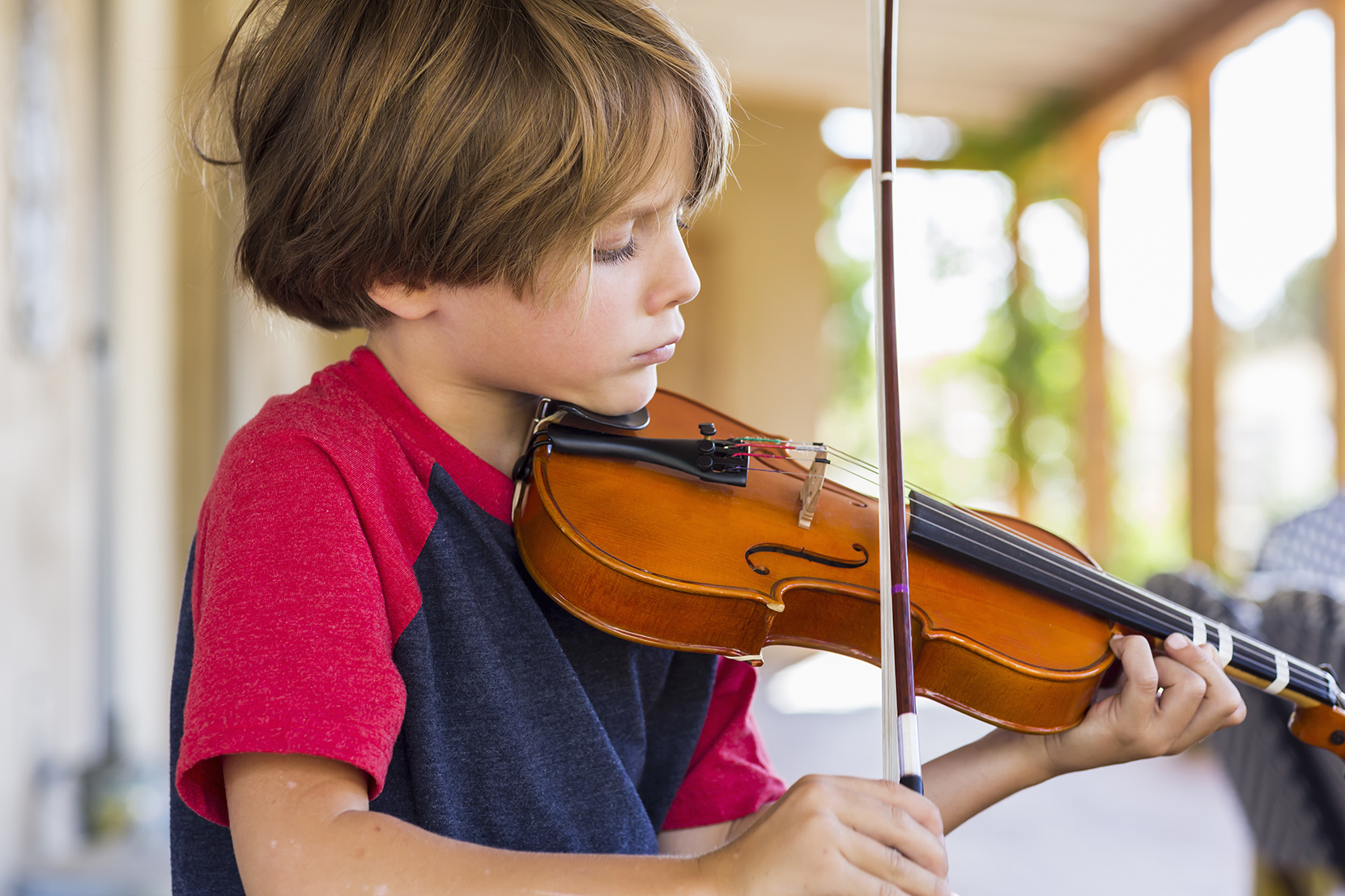 6 year old boy playing violin outside in garden