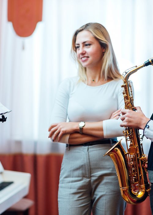 Cheerful teacher with student boy learning saxophone lessons at music school