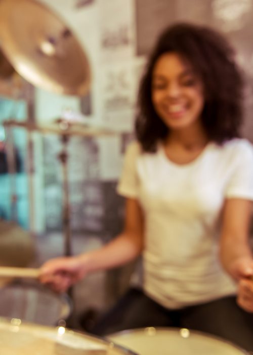 Beautiful Afro-American girl in white t-shirt smiling while playing drums in a musical shop